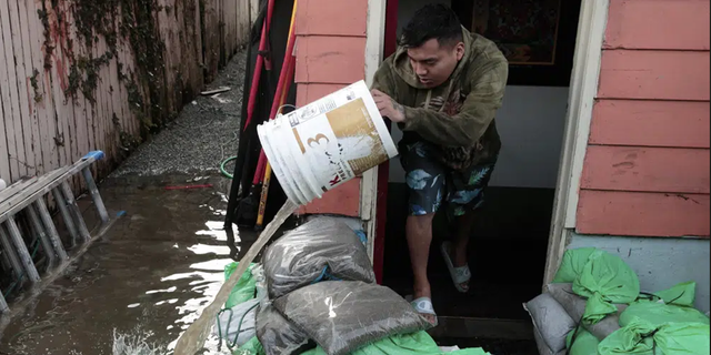 Manuel Israel Archila Lopez uses a bucket to scoop water from his family's home in Seattle's South Park neighborhood Tuesday morning, Dec. 27, 2022.