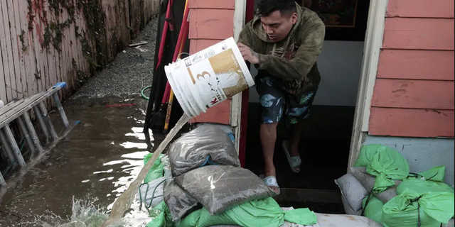 Manuel Israel Archila Lopez uses a bucket to scoop water from his family's home in Seattle's South Park neighborhood Tuesday morning, Dec. 27, 2022.