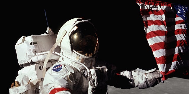 Apollo 17 astronaut Gene Cernan touches an American flag on the surface of the moon.