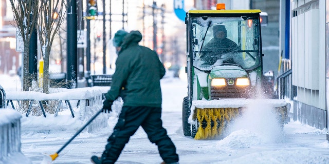 A man shovels the sidewalk while another one clears the snow with a power sweeper Thursday, Dec. 22, 2022 in downtown Minneapolis.