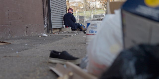 An addict sits on the corner in Kensington. The foreground is littered with trash and other junk — a common sight in the Philadelphia neighborhood.