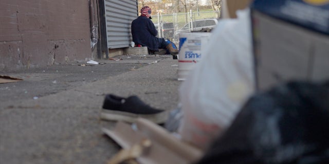 An addict sits on the corner in Kensington. The foreground is littered with trash and other junk — a common sight in the Philadelphia neighborhood.