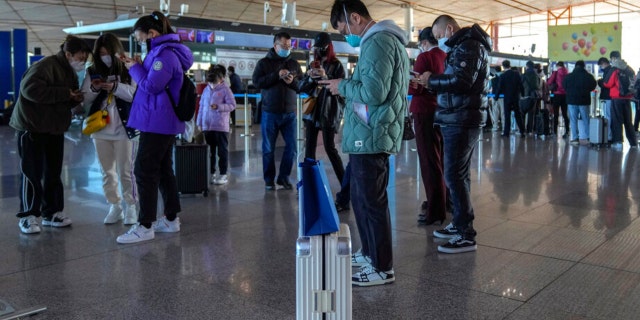 Masked travelers use their smartphones to fill in their health declaration after checking in at the international flight check in counter at the Beijing Capital International Airport in Beijing, Thursday, Dec. 29, 2022.