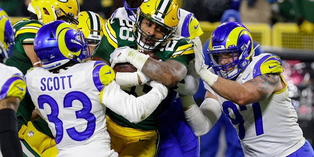 Green Bay Packers running back AJ Dillon (28) runs in for a touchdown between Los Angeles Rams cornerback Nick Scott (33) and defensive tackle Michael Hoecht (97) in the first half of an NFL football game in Green Bay, Wis. Monday, Dec. 19, 2022.