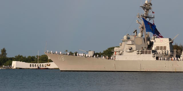 Sailors aboard the USS Daniel Inouye render honors while passing the USS Arizona Memorial and the sunken battleship the USS Arizona during a ceremony Wednesday, Dec . 7, 2022, in Pearl Harbor, Hawaii, in remembrance of those killed in the 1941 attack.