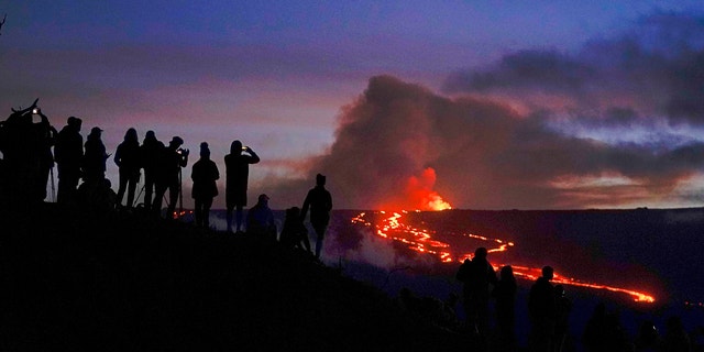 People watch and record images of lava from the Mauna Loa volcano Thursday, Dec. 1, 2022, near Hilo, Hawaii.