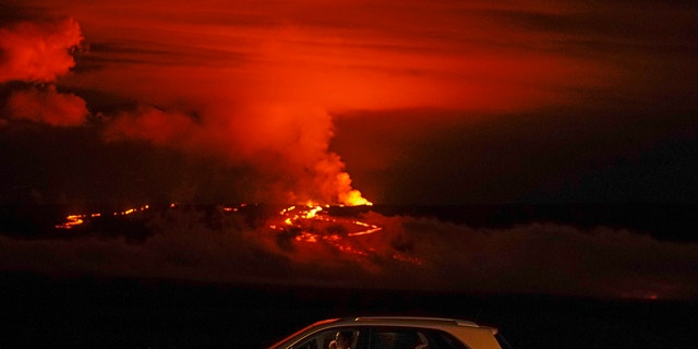 A man talks on a phone in his car alongside Saddle Road as the Mauna Loa volcano erupts Wednesday, Nov. 30, 2022, near Hilo, Hawaii. 