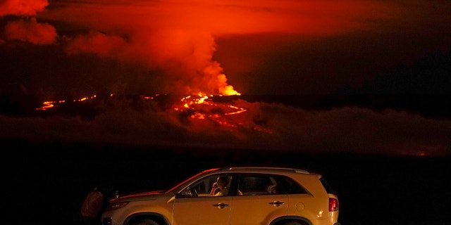 A man talks on a phone in his car alongside Saddle Road as the Mauna Loa volcano erupts Wednesday, Nov. 30, 2022, near Hilo, Hawaii.