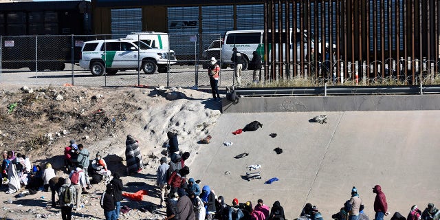 Migrants wait to cross the U.S.-Mexico border from Ciudad Juárez, Mexico, next to U.S. Border Patrol vehicles in El Paso, Texas, Wednesday, Dec. 14, 2022.