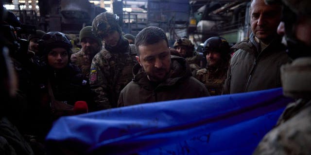 Ukrainian President Volodymyr Zelenskyy, signs a Ukraine national flag, at the site of the heaviest battles with the Russian invaders in Bakhmut, Ukraine, Tuesday, Dec. 20, 2022.