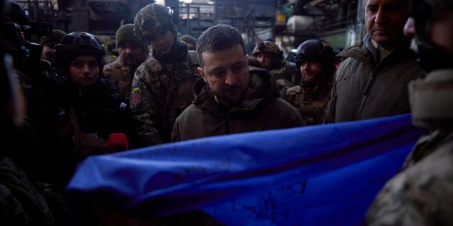 Ukrainian President Volodymyr Zelenskyy, signs a Ukraine national flag, at the site of the heaviest battles with the Russian invaders in Bakhmut, Ukraine, Tuesday, Dec. 20, 2022.