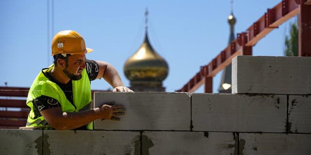 建設作業員は、2022 年 7 月 13 日水曜日、ウクライナ東部のドネツク人民共和国政府の管理下にある地域で、正教会を背景にマリウポリの新しい市立医療センターの現場で働いています。