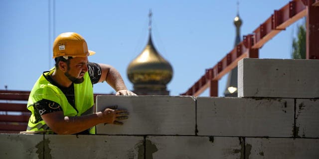 A construction worker works at the site of the new municipal medical center in Mariupol with an Orthodox church in the background, in a region controlled by the government of the Donetsk People's Republic, in eastern Ukraine, Wednesday, July 13, 2022.