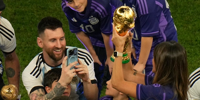 Argentina's Lionel Messi takes pictures of his wife Antonela Roccuzzo as she holds the trophy after Argentina won the World Cup over France in Lusail, Qatar, Sunday, Dec. 18, 2022.