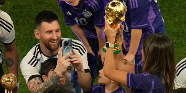 Argentina's Lionel Messi takes pictures of his wife Antonela Roccuzzo as she holds the trophy after Argentina won the World Cup over France in Lusail, Qatar, Sunday, Dec. 18, 2022.