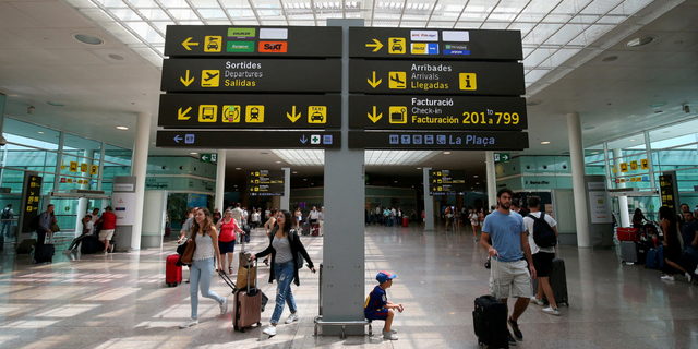 People walk under a sign at Barcelona's El Prat airport in Spain pn Aug. 4, 2017.