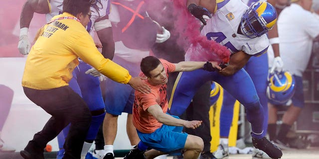 A fan with a smoke bomb is tackled on the field by Los Angeles Rams' Bobby Wagner, #45, Takkarist McKinley, #50, and a security guard during their NFL game against the San Francisco 49ers at Levis Stadium in Santa Clara, California, on Monday, Oct. 3, 2022. 