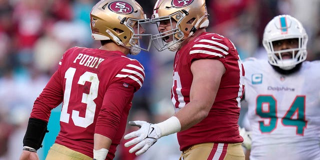 San Francisco 49ers quarterback Brock Purdy, #13, celebrates after throwing a touchdown pass to running back Christian McCaffrey with offensive tackle Daniel Brunskill, middle, as Miami Dolphins defensive tackle Christian Wilkins, #94, reacts during the first half of an NFL football game in Santa Clara, California, Sunday, Dec. 4, 2022. 