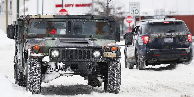 A National Guard truck drives past a police cruiser on a snowy street in Buffalo, N.Y., on Tuesday, Dec. 27, 2022. 