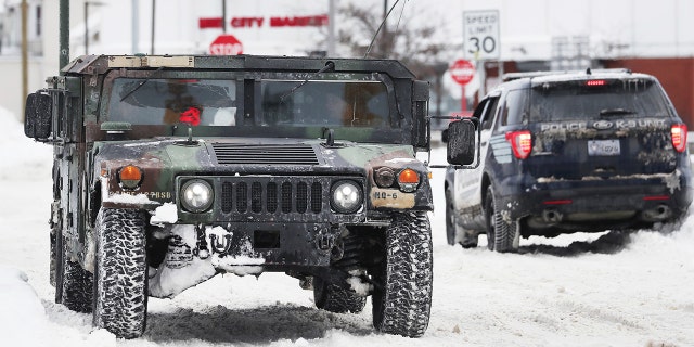 A National Guard truck drives past a police cruiser on a snowy street in Buffalo, N.Y., on Tuesday, Dec. 27, 2022. 