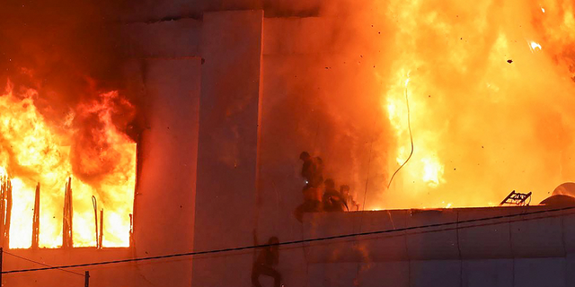 Fire burns around people on a ledge on the side of the Grand Diamond City casino and hotel in Poipet, Cambodia on Dec. 29.