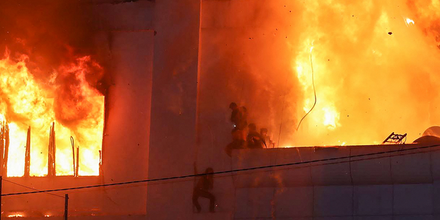 Fire burns around people on a ledge on the side of the Grand Diamond City casino and hotel in Poipet, Cambodia on Dec. 29.