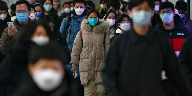 Masked commuters walk through a walkway in between two subway stations as they head to work during the morning rush hour in Beijing, Tuesday, Dec. 20, 2022.