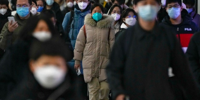 Masked commuters walk through a walkway in between two subway stations as they head to work during the morning rush hour in Beijing, Tuesday, Dec. 20, 2022.