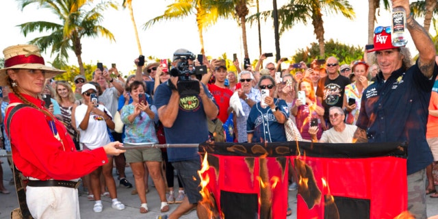 Jai Somers holds burning hurricane flags after they were doused with rum and set on fire to mark the end of the 2022 Atlantic hurricane season, Wednesday, Nov. 30, 2022, in Key West, Florida.