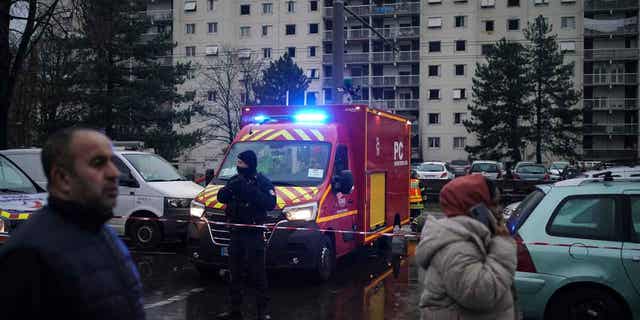 A police officer stands by a firefighter truck next to apartment buildings in Vaulx en Velin, outside Lyon, central France, on Dec. 16, 2022. French authorities say 10 people died in the fire.