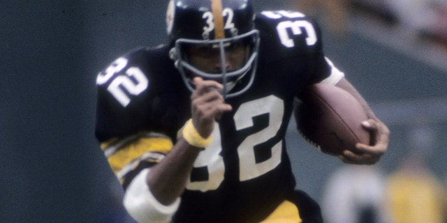 Franco Harris, número 32 de los Pittsburgh Steelers, juega sosteniendo el balón contra los Denver Broncos a mediados de la década de 1970 durante un partido de fútbol americano de la NFL en el Three Rivers Stadium de Pittsburgh.  Harris jugó para los Steelers de 1972 a 1983.