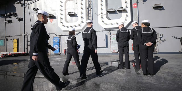 U.S. sailors walk with the flag on the flight deck of the USS Nimitz in Coronado, California, on Jan. 18, 2020.