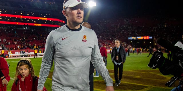 El entrenador en jefe de la USC, Lincoln Riley, sostiene la mano de su hija mientras sale del campo después de que los troyanos vencieran a Notre Dame en el Coliseo el 26 de noviembre de 2022 en Los Ángeles.