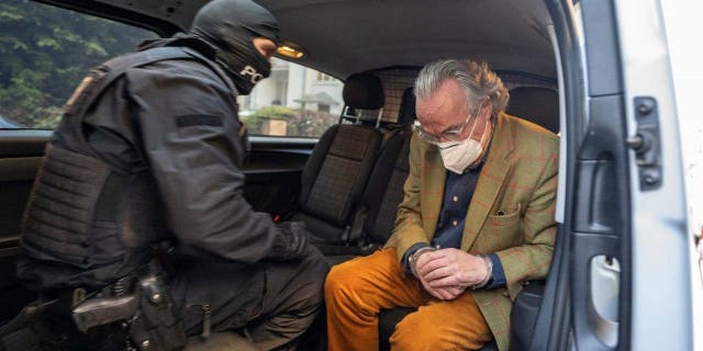 During a raid in Frankurt, Germany, against so-called "Reich citizens," a hooded police officer sits in a police vehicle with the arrested Heinrich XIII Prince Reuss, right, after searching a house, Dec. 7, 2022.