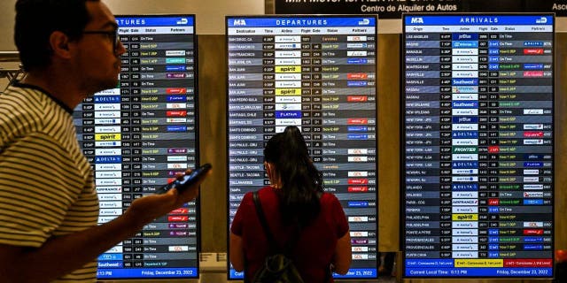 Travelers look at flight schedules at Miami International Airport during a winter storm ahead of the Christmas holiday in Miami, Florida, on December 23, 2022. - Nearly a million-and-a-half US power customers were in the dark Friday as a severe winter storm walloped the country, causing highway closures and thousands of flight cancellations days before Christmas. Heavy snow, howling winds, and air so frigid it instantly turned boiling water into ice took hold of much of the nation, including normally temperate southern states. (Photo by CHANDAN KHANNA / AFP) 