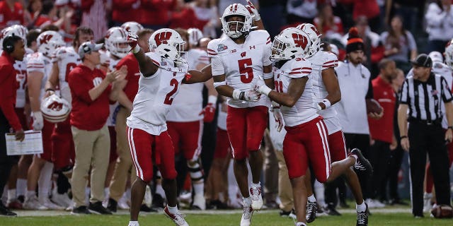 El esquinero de los Wisconsin Badgers, Cedrick Dort Jr., No. 5, celebra una intercepción con sus compañeros de equipo durante el partido de fútbol americano universitario de tasa garantizada entre los Wisconsin Badgers y los Oklahoma State Cowboys el 27 de diciembre de 2022 en el Chase Field de Phoenix.