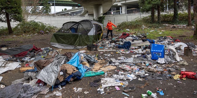 A woman dismantles a tent as garbage lies piled at a homeless encampment on March 13, 2022 in Seattle. The accumulation of garbage at such sites has become a major issue in Seattle as the city tries to move the unhoused out of shared public spaces. 