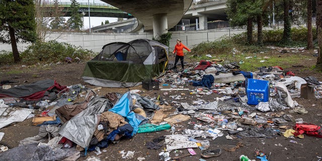 A woman dismantles a tent as garbage lies piled at a homeless encampment on March 13, 2022 in Seattle. The accumulation of garbage at such sites has become a major issue in Seattle as the city tries to move the unhoused out of shared public spaces. 