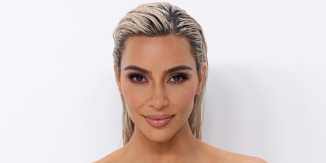 Kim Kardashian with a slicked back blonde hair-do smiles for a photo