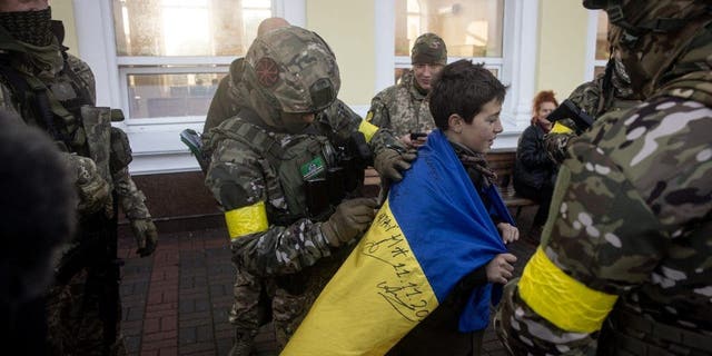 A boy has his Ukraine national flag signed by members of the Ukrainian military on the train platform prior to the arrival of the first train back in Kherson train station since Russian forces retreated on Nov. 19, 2022, in Kherson, Ukraine. 