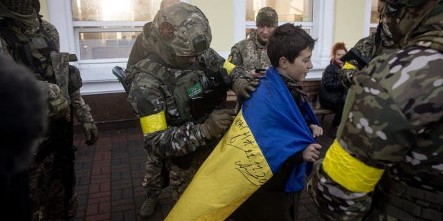 A boy has his Ukraine national flag signed by members of the Ukrainian military on the train platform prior to the arrival of the first train back in Kherson train station since Russian forces retreated on Nov. 19, 2022, in Kherson, Ukraine.