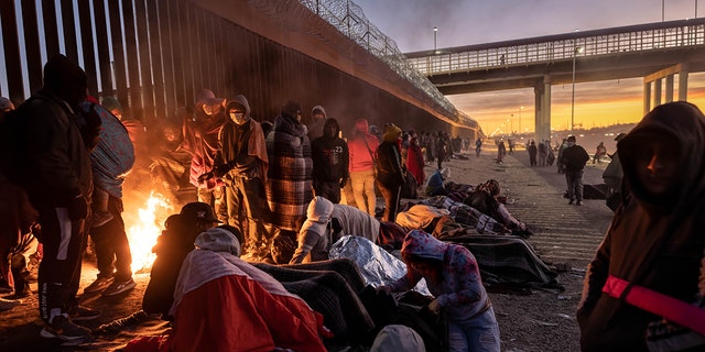 Immigrants warm to a fire at dawn after spending the night outside next to the U.S.-Mexico border fence on December 22, 2022 in El Paso, Texas.