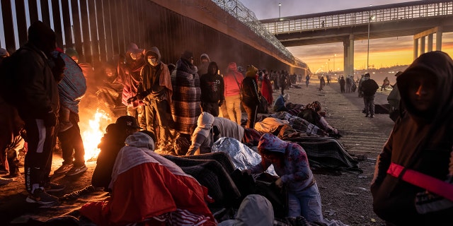 Inmigrantes se calientan frente a una fogata al amanecer después de pasar la noche afuera junto a la valla fronteriza entre Estados Unidos y México el 22 de diciembre de 2022 en El Paso, Texas.