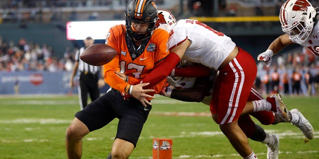 El mariscal de campo de los Oklahoma State Cowboys, Garret Rangel, No. 13, pierde el balón fuera de los límites después de ser tocado por el esquinero de los Wisconsin Badgers, Avyonne Jones, No. 8, durante la segunda mitad del Guaranteed Rate Bowl en Chase Field el 27 de diciembre.  2022 en Fénix.