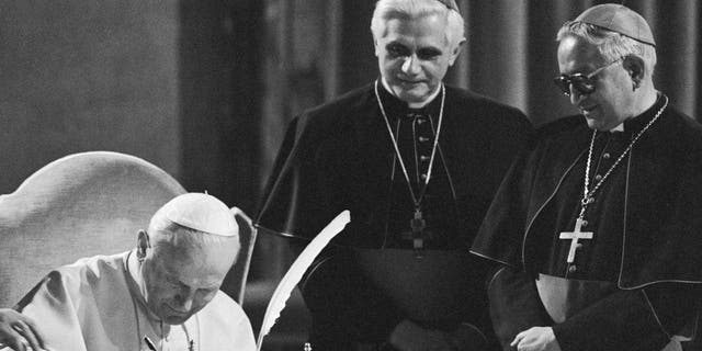 Pope John Paul II, seated at a table in the Old Consistorial Hall, signs the new Roman Catholic Code of Canon Law during a ceremony at the Vatican 1/25; in center West German Cardinal Joseph Ratzinger, and at right Venezuelan Archbishop Rosalio Jose Castillo Lara, Chairman of the Vatican commission that has been revising the code for the last two decades. The new Code of Canon Law is a more streamlined set of Church law that retains automatic excommunication for abortion and makes marriage annulments more complex.