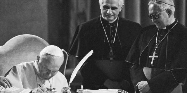 Pope John Paul II, seated at a table in the Old Consistorial Hall, signs the new Roman Catholic Code of Canon Law during a ceremony at the Vatican 1/25; in center West German Cardinal Joseph Ratzinger, and at right Venezuelan Archbishop Rosalio Jose Castillo Lara, Chairman of the Vatican commission that has been revising the code for the last two decades. The new Code of Canon Law is a more streamlined set of Church law that retains automatic excommunication for abortion and makes marriage annulments more complex.