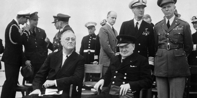 President Roosevelt and Prime Minister Churchill are shown on the big forward deck of H.M.S. Prince of Wales as they relax, chat and breathe a bit of salt air during their epoch-making Atlantic meeting on March 15, 1941. Behind the two at right are: Admiral E.J. King, commander of the U.S. Atlantic Fleet, and Gen. George C. Marshall (far right).