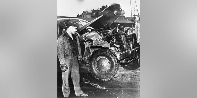 PFC. Horace L. Woodring, 19, Sturgis, Kentucky, General Patton's chauffeur, is shown looking at the smashed-in front of Gen. Patton's car. Woodring and the driver of the truck that crashed into the car were sent back to their outfits with no disciplinary action because previous records revealed that both were excellent drivers.