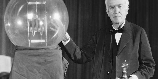 Thomas A. Edison, in this photo, exhibits a replica of his first successful incandescent lamp, which gave 16 candlepower of illumination, in contrast to the ultimate in today's achievement, a 50,000-watt, 150,000-candlepower lamp.