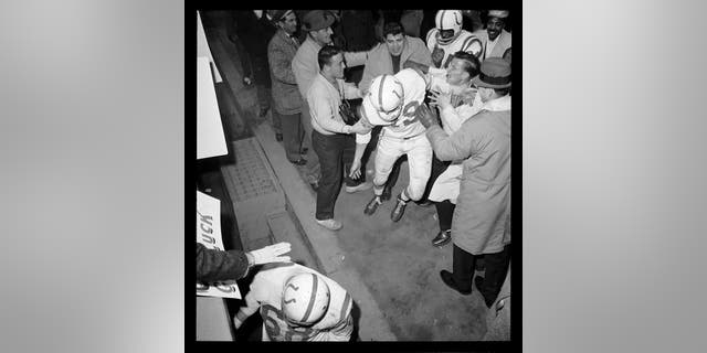 Baltimore Colts quarterback Johnny Unitas is mobbed by well-wishers as he heads for the dressing room after leading the Colts to a 23-17 win over the New York Giants in the first "sudden death" overtime in National Football history. Unitas set a record of 349 yards gained on passes in a title game.